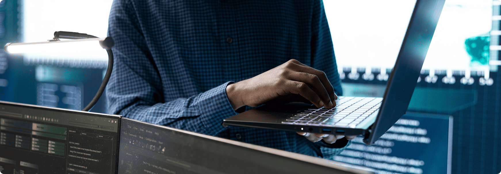 Ingénieur en sécurité informatique travaillant sur un ordinateur portable devant des écrans de contrôle de données